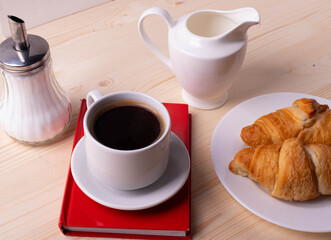 a white ceramic cup with black espresso, french croissant as breakfast or snack concept on rustic, natural texture wooden surface