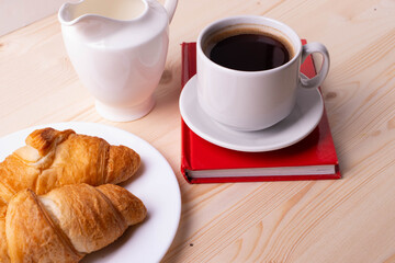 a white ceramic cup with black espresso, french croissant as breakfast or snack concept on rustic, natural texture wooden surface