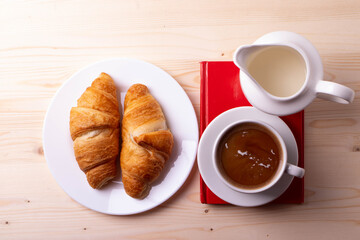 a white ceramic cup with black espresso, french croissant as breakfast or snack concept on rustic, natural texture wooden surface