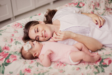Happy loving young mom with her baby at home on the bed. Newborn baby and mother together. Motherhood livestyle. Childhood. Tenderness care. Caucasian woman and child.  Bedroom