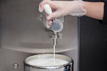 Hand with gloves filling the fresh milk from a tank