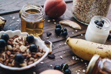 Healthy breakfast ingredients. Homemade granola, oatmeal, yogurt in the bottle, honey, berries and fruits on a wooden background. Morning aesthetics and beautiful layout on a wooden table.