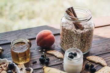 Healthy breakfast ingredients. Homemade granola, oatmeal, yogurt in the bottle, honey, berries and fruits on a wooden background. Morning aesthetics and beautiful layout on a wooden table.