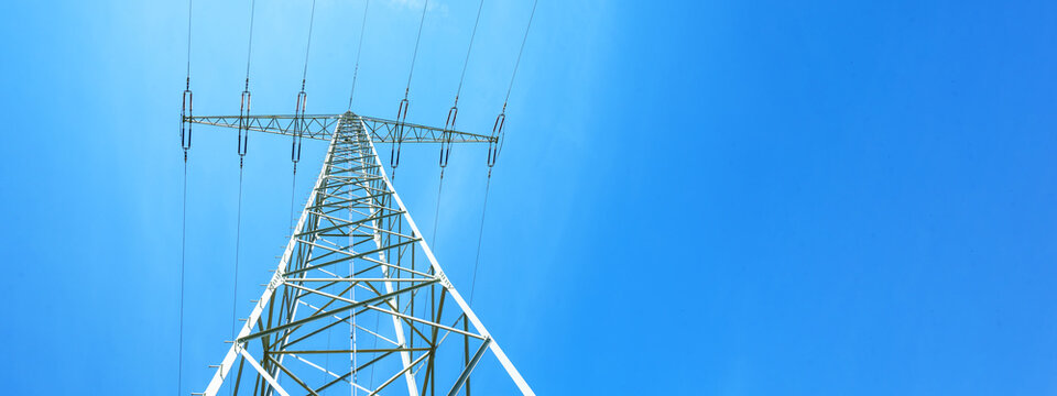 Electricity background banner panorama - Voltage power lines / high voltage electric transmission tower with blue sky and shining sun