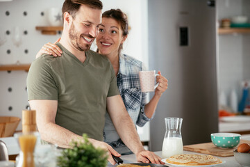 Young couple making pancakes together at home. Loving couple having fun while cooking.	
