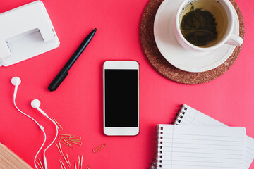 Smartphone, cup of green tea, notebooks, pen, paper clips, hole punch and earphones on pink background, flat lay. Education or working concept