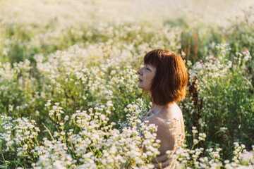 Fototapeta na wymiar European nude mature woman with bare shoulders with sensitive skin, freckles enjoys sunset in summer meadow.