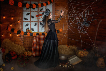 A sorceress in a black dress in a crown with a veil holds a magic ball in her hands. Pumpkins are licking on the floor, an old witch's book, and a broomstick stands against the wall. Fantasy 