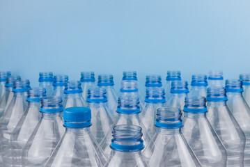 Empty clear plastic bottles with caps stacked on a blue background. Recycling and environment concept.