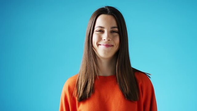 Studio portrait of confident smiling young woman laughing against blue background - shot in slow motion