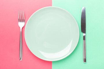 Empty mint plate, knife and fork on colored paper background Copy space Top view