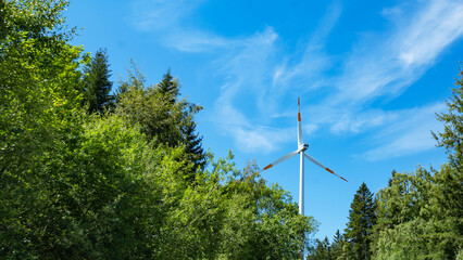 Wind power background - Blue cloudy sky with many windmill / wind turbines and green trees in the...