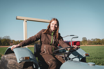 Junge Frau mit Spass an der Landwirtschaft sitzt auf einem Oldtimer - Traktor.