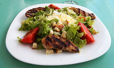 Caesar salad with chicken and cheese on a large white plate.