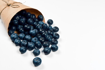 Freshly juicy picked blueberries in craft paper bag isolated on white background. Top view. Selective focus. Copy space. Concept of healthy eating and nutrition..