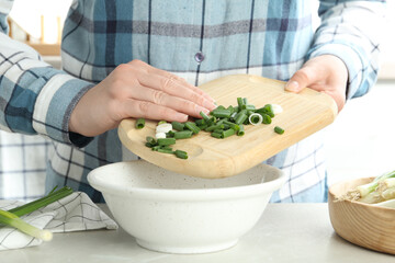 Woman putting chopped green spring onion into bowl on table, closeup