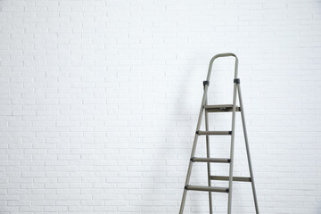 Metal stepladder near white brick wall. Space for text