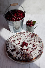 Clafoutis cherry pie, bucket and mug with cherries on gray wooden background.