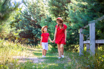 Fototapeta premium young mother in a red dress with her son walking in nature