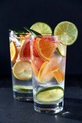 Health care, fitness, healthy nutrition diet concept. Fresh cool homemade citrus infused detox water with grapefruit, orange, lemon and lime and ice in glasses on dark background.