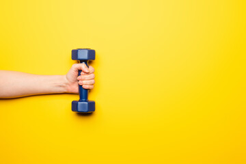 Fototapeta na wymiar cropped view of woman holding blue dumbbell on yellow background