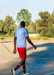 Fototapeta na wymiar Young African American athlete in a white t-shirt and red shorts walking calmly after jogging in a sports stadium. Man doing outdoor workout. Sport. People active lifestyle concept