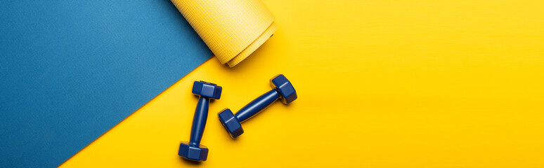 top view of blue fitness mat with dumbbells on yellow background, panoramic shot