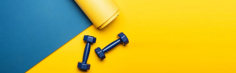 Gordijnen top view of blue fitness mat with dumbbells on yellow background, panoramic shot © LIGHTFIELD STUDIOS