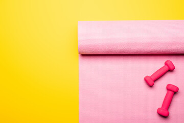 top view of pink fitness mat and dumbbells on yellow background