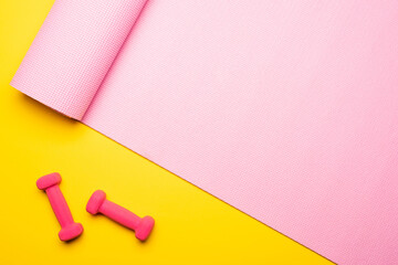 top view of pink fitness mat and dumbbells on yellow background