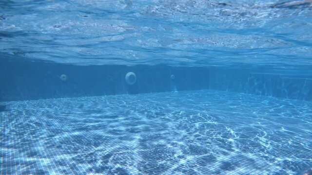 SLOW M - Bottom of the swimming pool. Clear water background with the reflection of sun rays underwater. Amazing view from underwater camera. Inflowing water jet into a swimming pool with blue tiles. 