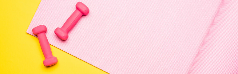 top view of pink fitness mat and dumbbells on yellow background, panoramic shot