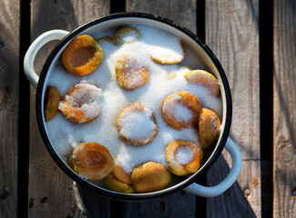 A saucepan with apricot halves, covered with sugar for making jam, on a table in the garden