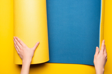 partial view of woman rolling out blue fitness mat on yellow background