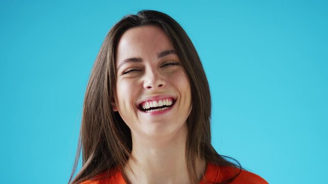 Studio portrait of confident smiling young woman laughing against blue background - shot in slow motion