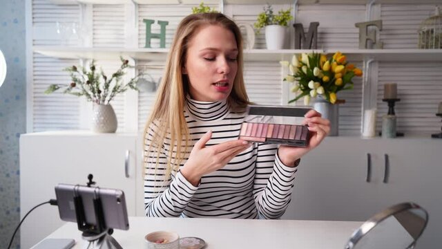 Beauty blogger woman filming daily makeup routine tutorial near camera. Influencer girl live streaming cosmetics product review. Vlogger female recommends eye shadow palette, teaches in masterclass.