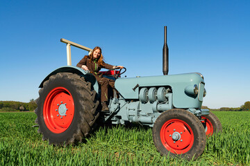 Junge Frau mit Spass an der Landwirtschaft sitzt auf einem Oldtimer - Traktor.
