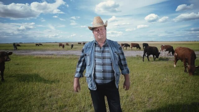 Portrait of a farmer surrounded by a herd of bulls. Shepherd in a straw hat on a pasture. Herd owner. Farmer in a cowboy hat and denim vest.