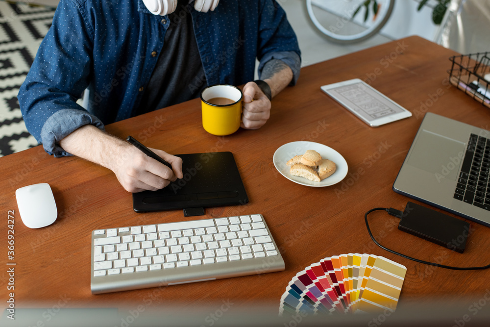 Wall mural close-up of unrecognizable graphic artist sitting at wooden desk and using digitizer while creating 