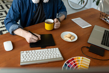 Close-up of unrecognizable graphic artist sitting at wooden desk and using digitizer while creating layout