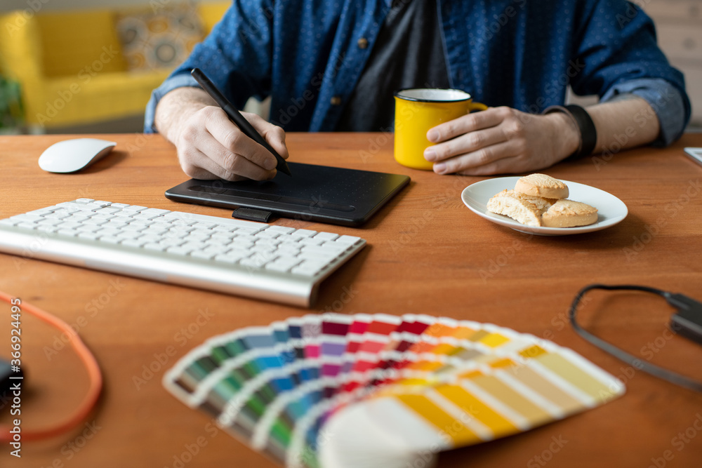 Wall mural close-up of unrecognizable graphic designer sitting at table with mug and cookies on plate and worki