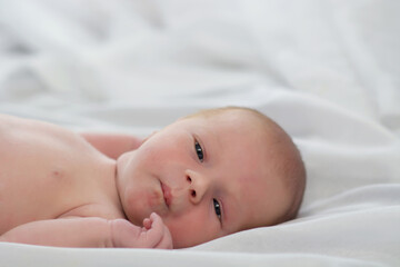 Portrait of a cute newborn baby looking into the camera. Little boy 7 days, one week. The baby lies on a white silk blanket. Copyspace