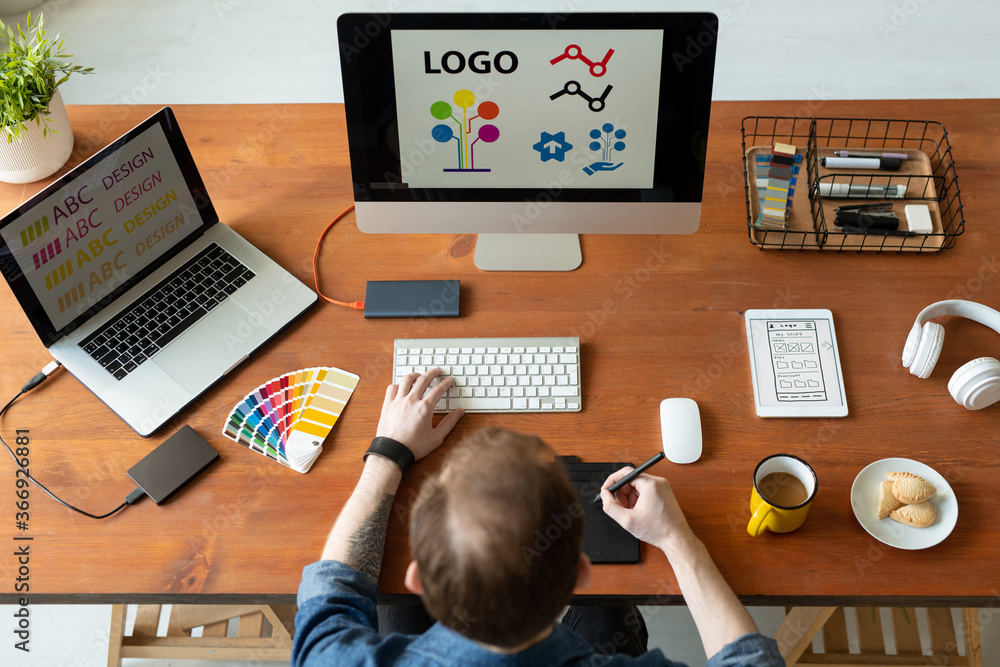 Wall mural above view of logo designer sitting at desk and editing icon design using drawing pad