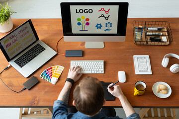Above view of logo designer sitting at desk and editing icon design using drawing pad