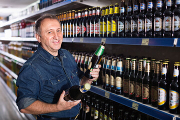 Portrait of a cheerful elderly man buying a beer at the grocery store