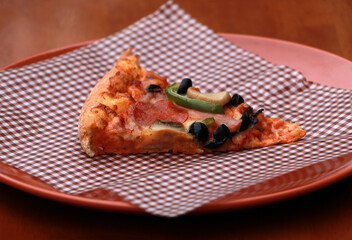 A piece of triangle Pizza  place on brown scotch paper  in the brown round plate.