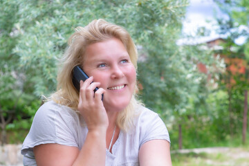 Portrait of a blond smiling woman talking on the phone against the background of nature.