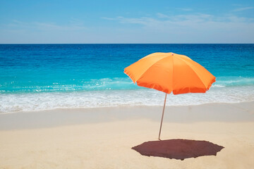 Single orange umbrella on a perfect beach with clean golden sand and clear turquoise water on a windless and sunny summer day. Tropical background, copy space, top view.