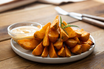 Fried potato chips with herbs and sauce in white plate, golden roasted potatoe slices with herbs.