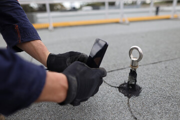 Inspector auditor technician using his phone photographing fall arrest, fall restraint roof anchor point
horizontal safety line while conducting yearly safety inspection prior used     